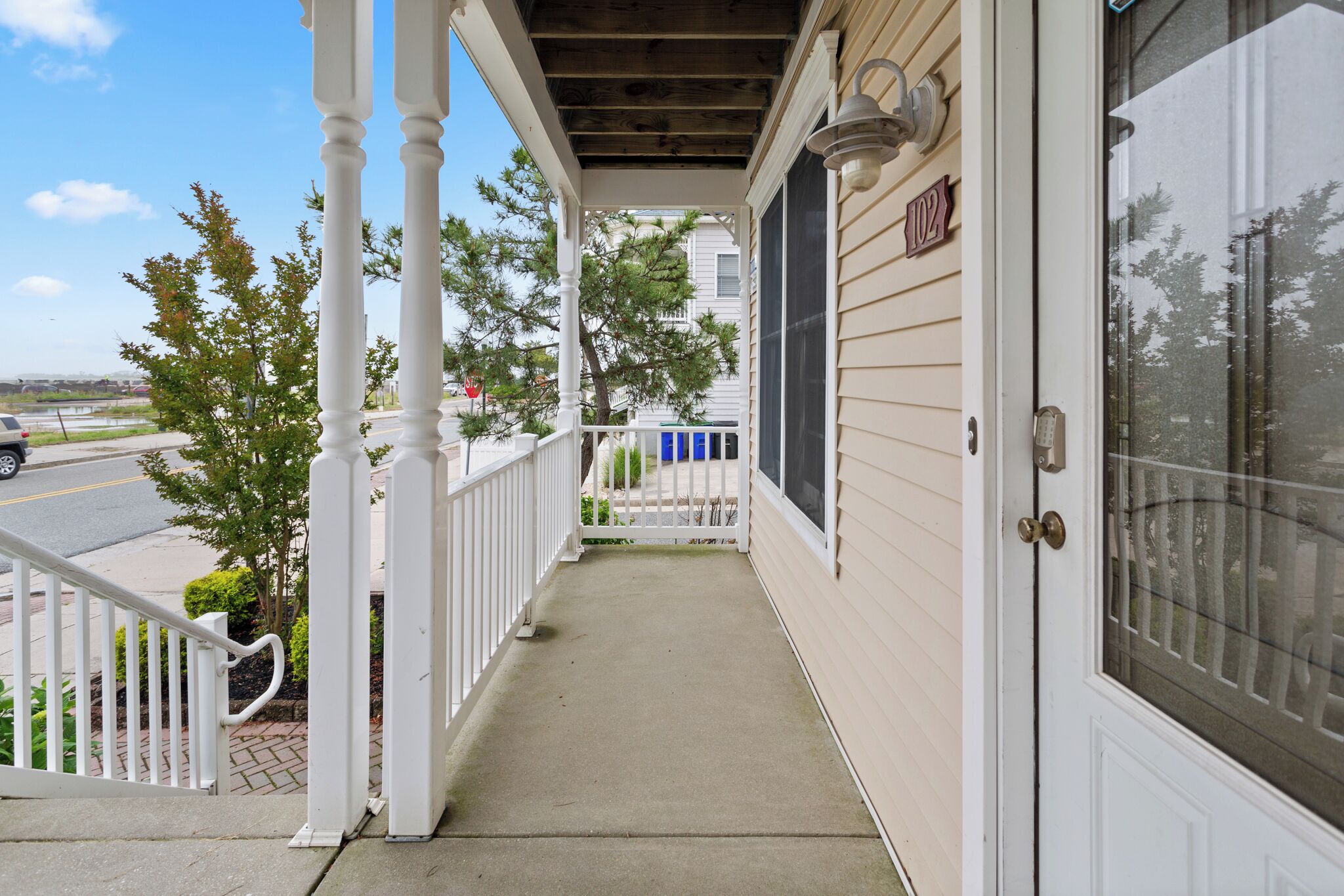 A covered porch with a white railing, a door with a number, and a view of the street.