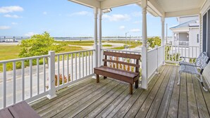 A wooden deck with a bench and a metal chair, overlooking a grassy area and a bridge.