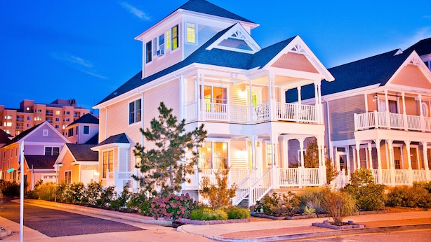 A two-story house with a balcony and a porch, surrounded by other houses.