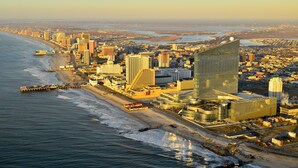 Un paisaje urbano costero con modernos edificios altos, un muelle que se adentra en el océano, y una vista despejada de la playa y el agua.