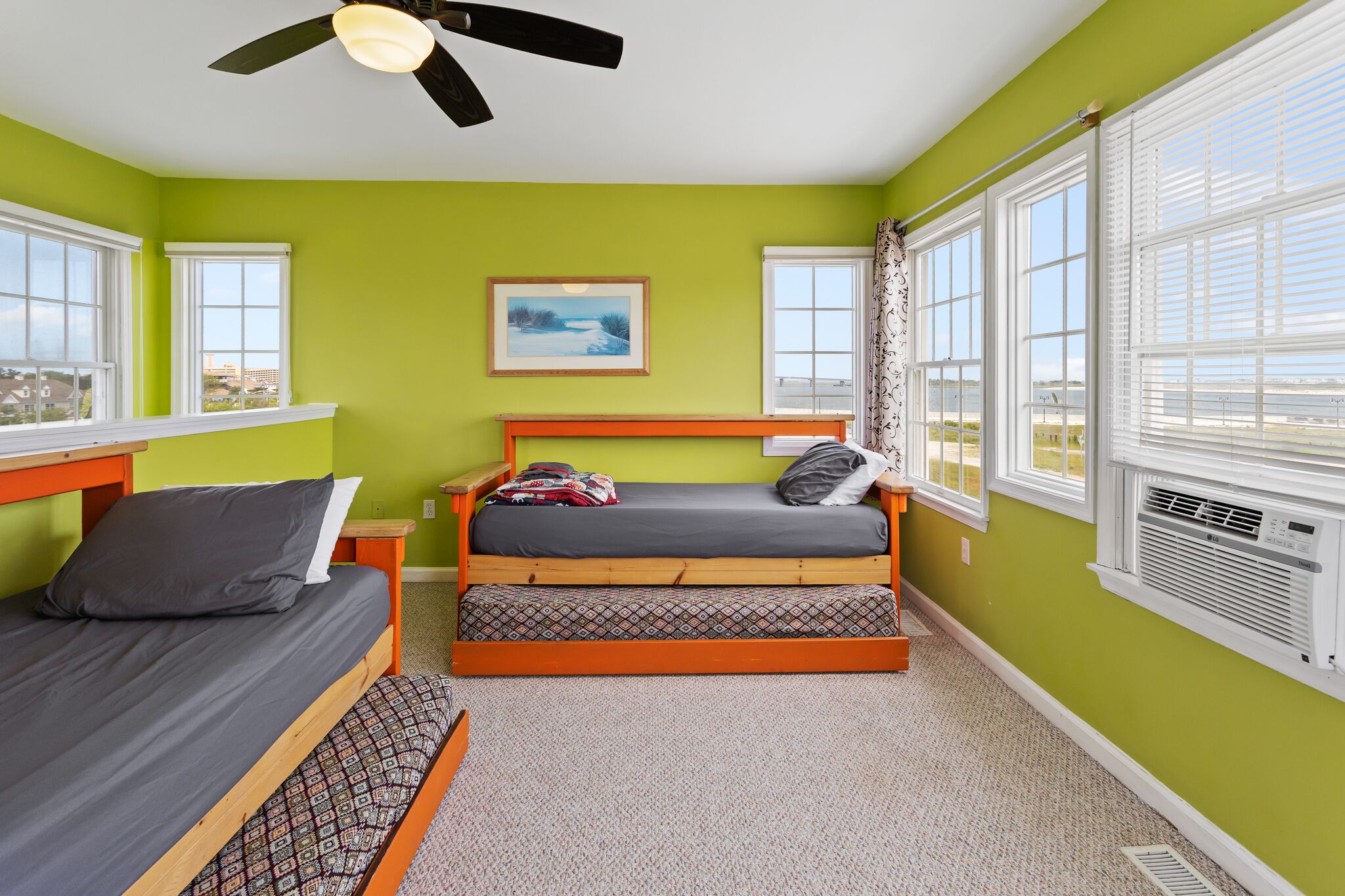A room with two beds, a ceiling fan, a window with blinds, and a framed picture on the wall.