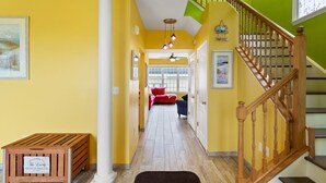 A hallway with a wooden bench, a staircase, and a view into a living area with a red couch and a blue chair.