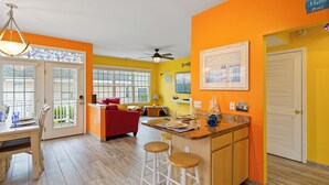 A bright kitchen with a central island, a dining area with a table and chairs, and a red sofa.