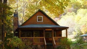 Une cabane dotée d’une véranda, entourée d’arbres et de feuillage.