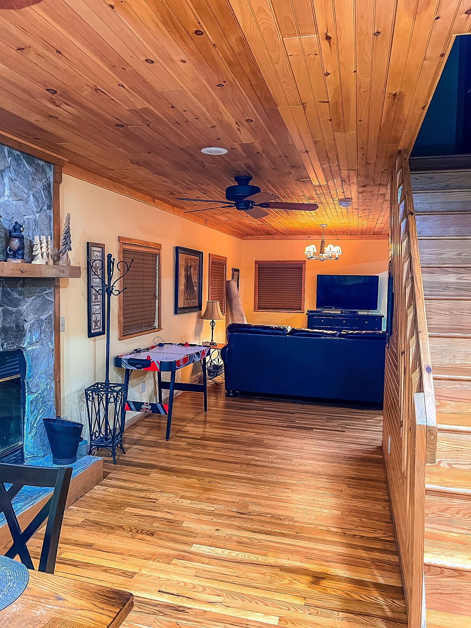Un salon chaleureux avec une cheminée, un plancher en bois, un canapé, un téléviseur et un ventilateur de plafond.