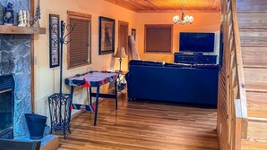 Een gezellige woonkamer met een open haard, houten vloeren, een bank, een televisie en een plafondventilator.