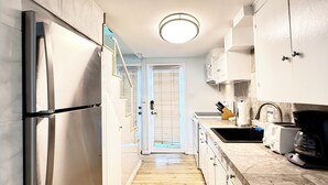 A narrow kitchen with white cabinets, a stainless steel refrigerator, a coffee maker, and a sink. - 2BD Home, 1/2 Block to the Beach, A/C, Pet Friendly, WIFI. - 124 Claressa Ave (Avalon)