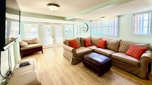 A spacious living room with a sectional sofa, ottoman, and a television. - 2BD Home, 1/2 Block to the Beach, A/C, Pet Friendly, WIFI. - 124 Claressa Ave (Avalon)