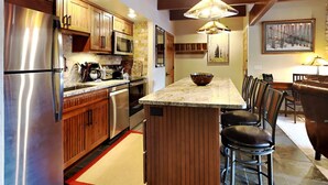 Una cocina moderna con electrodomésticos de acero inoxidable, armarios de madera y una isla central con taburetes de bar.