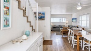 A spacious living area with a wooden dining table, white chairs, a sofa, and a staircase with white railings. - 324D: Well-appointed Two Story Home + Ample Deck + WIFI + New Carpet - 324 Desca (Avalon)