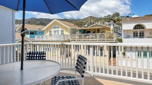 A balcony with a table and chairs, a blue umbrella, and a view of houses and mountains. - 324D: Well-appointed Two Story Home + Ample Deck + WIFI + New Carpet - 324 Desca (Avalon)