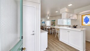 A modern kitchen with white cabinetry, a wooden dining table, and a large window with blinds. - 324D: Well-appointed Two Story Home + Ample Deck + WIFI + New Carpet - 324 Desca (Avalon)