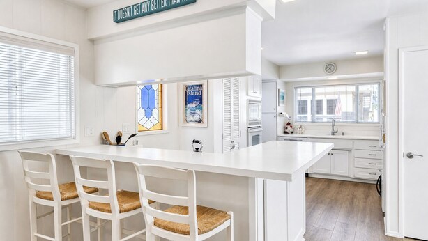 A modern kitchen with a white island, bar stools, and a sign above. - 324D: Well-appointed Two Story Home + Ample Deck + WIFI + New Carpet - 324 Desca (Avalon)