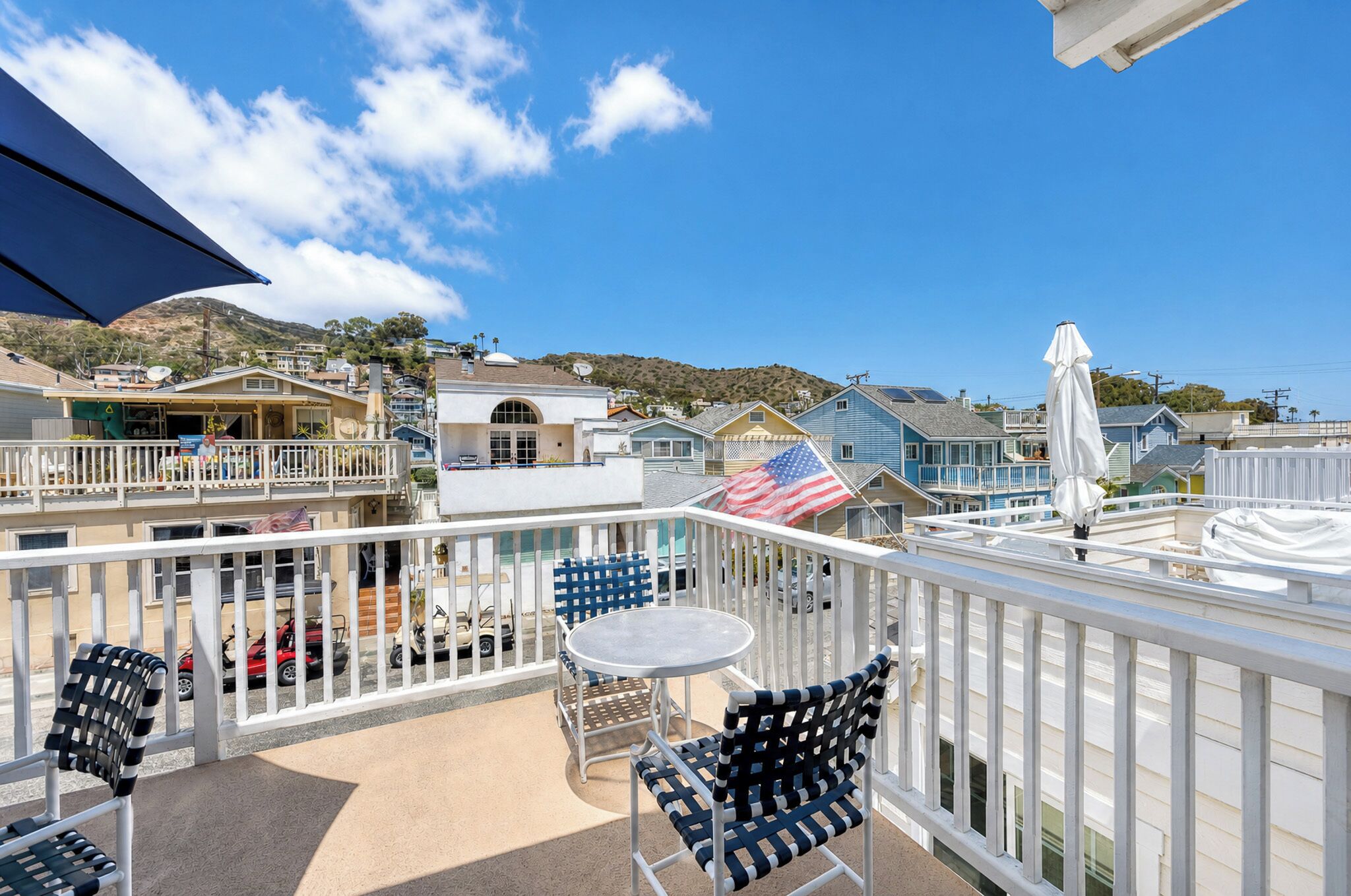 A balcony with outdoor seating, a view of the surrounding neighborhood, and a clear blue sky.