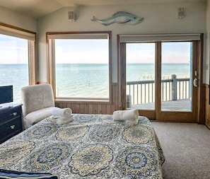 A bedroom with a large bed, two windows, a balcony with a view of the sea, and a decorative fish on the wall.