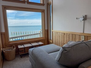 Ein Zimmer mit großem Fenster mit Blick auf einen hölzernen Steg und das Meer.