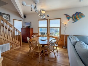 A dining area with a wooden table and chairs, a wooden staircase, and a view through large windows.