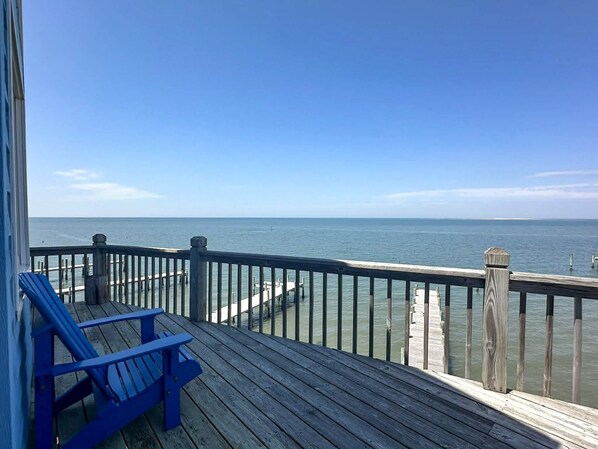 A wooden deck with a railing, a blue chair, and a view of the ocean.