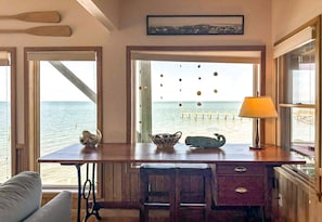 A room with a view of the sea, a wooden desk with a lamp, and a chair.