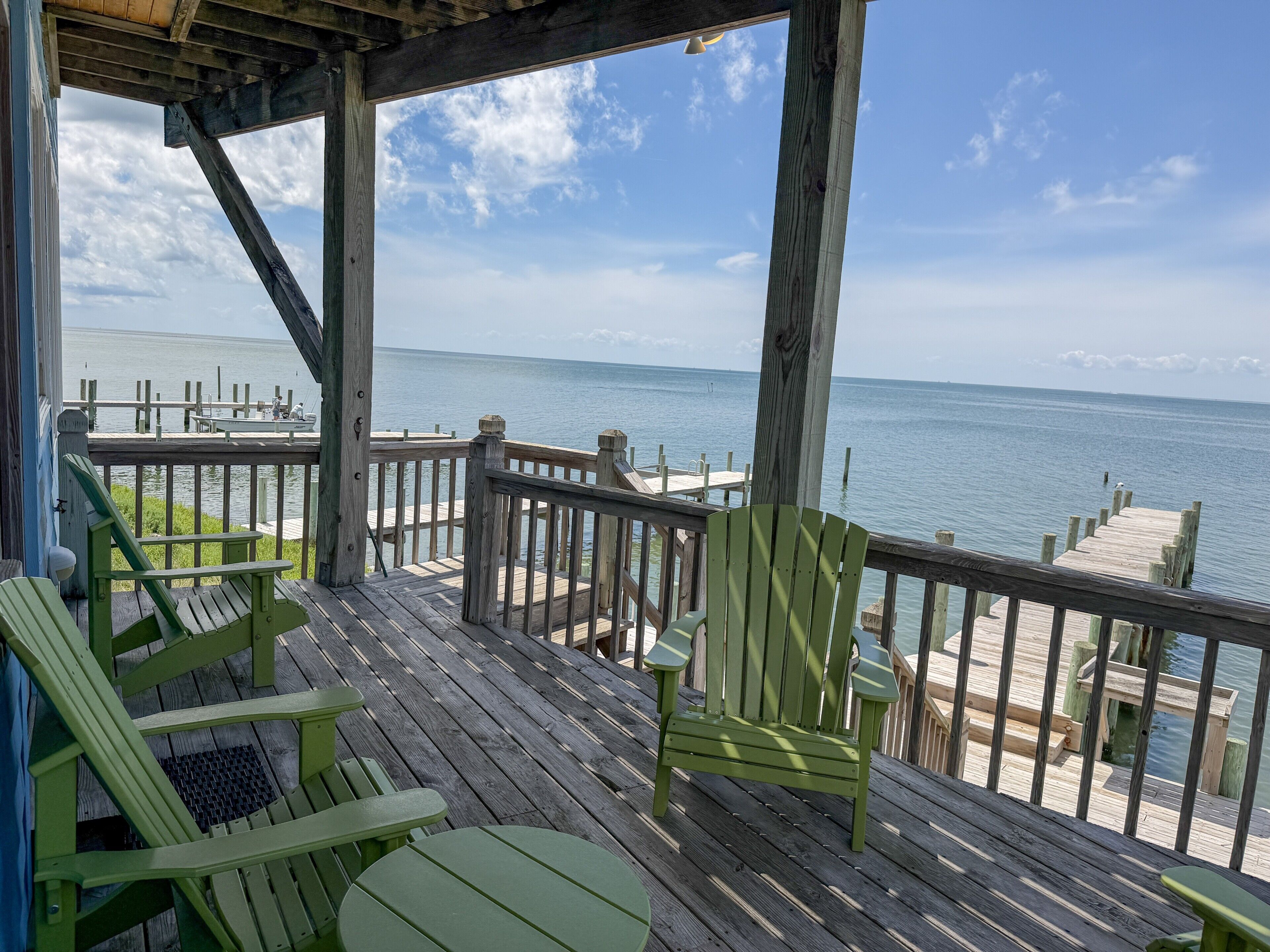 A wooden deck with green Adirondack chairs overlooking a calm body of water.