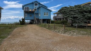 A two-story house with a gravel driveway leading to a wooden dock. - Out Of The Blue: Soundfront, spectacular sunsets, private boat dock. (Ocracoke)