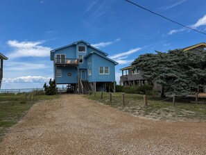 A two-story house with a gravel driveway leading to a wooden dock. - Out Of The Blue: Soundfront, spectacular sunsets, private boat dock. (Ocracoke)