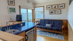 A compact kitchen with a built-in dishwasher, a wooden dining table, and a blue countertop. - Out Of The Blue: Soundfront, spectacular sunsets, private boat dock. (Ocracoke)