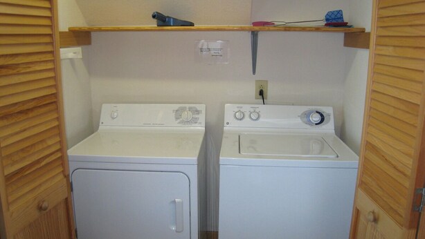 A laundry room with two white washing machines and a shelf above them. - Out Of The Blue: Soundfront, spectacular sunsets, private boat dock. (Ocracoke)