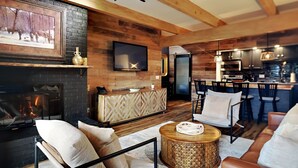 Ein modernes Wohnzimmer mit Kamin, Holzwänden, einem Fernseher und einer Küchenzeile mit Barhockern.