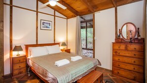 Una camera da letto con soffitto in legno, un letto con coperta verde, due lampade da comodino, un comò in legno e una finestra con tende.