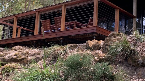 Un patio in legno con posti a sedere all'aperto, circondato da vegetazione e rocce naturali.
