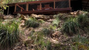 Una terrazza in legno rustico con ringhiere in metallo, immersa nel verde tra vegetazione e alberi.