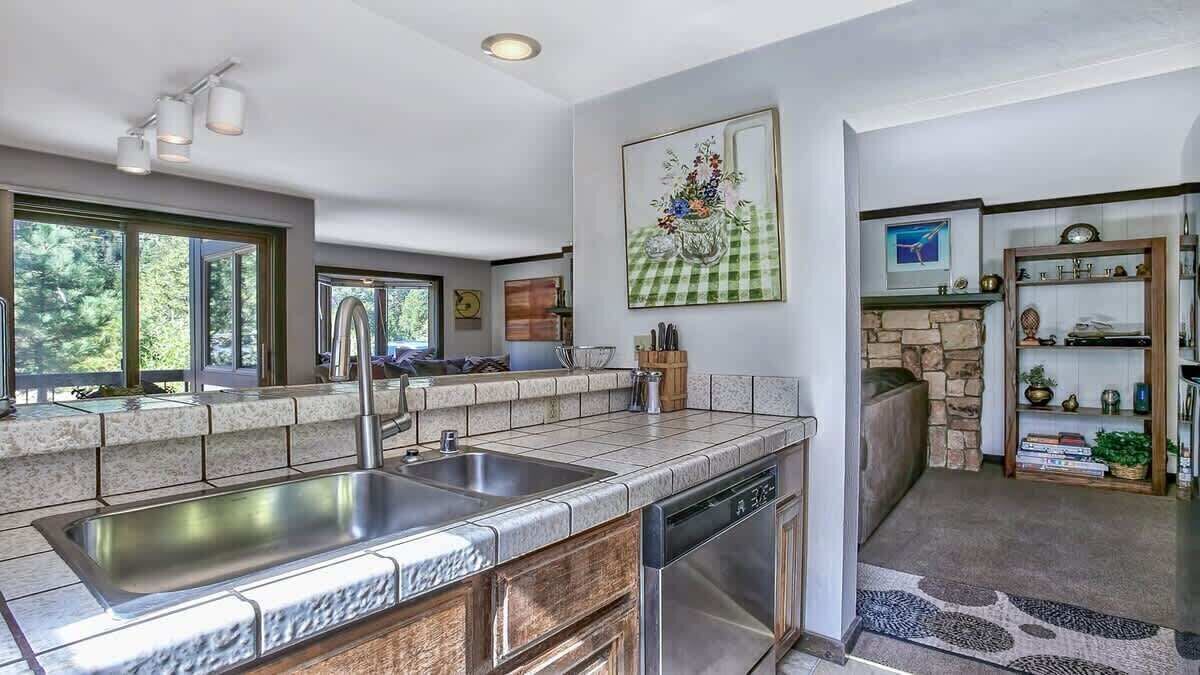 A modern kitchen with a built-in dishwasher, large windows, and a stone fireplace.