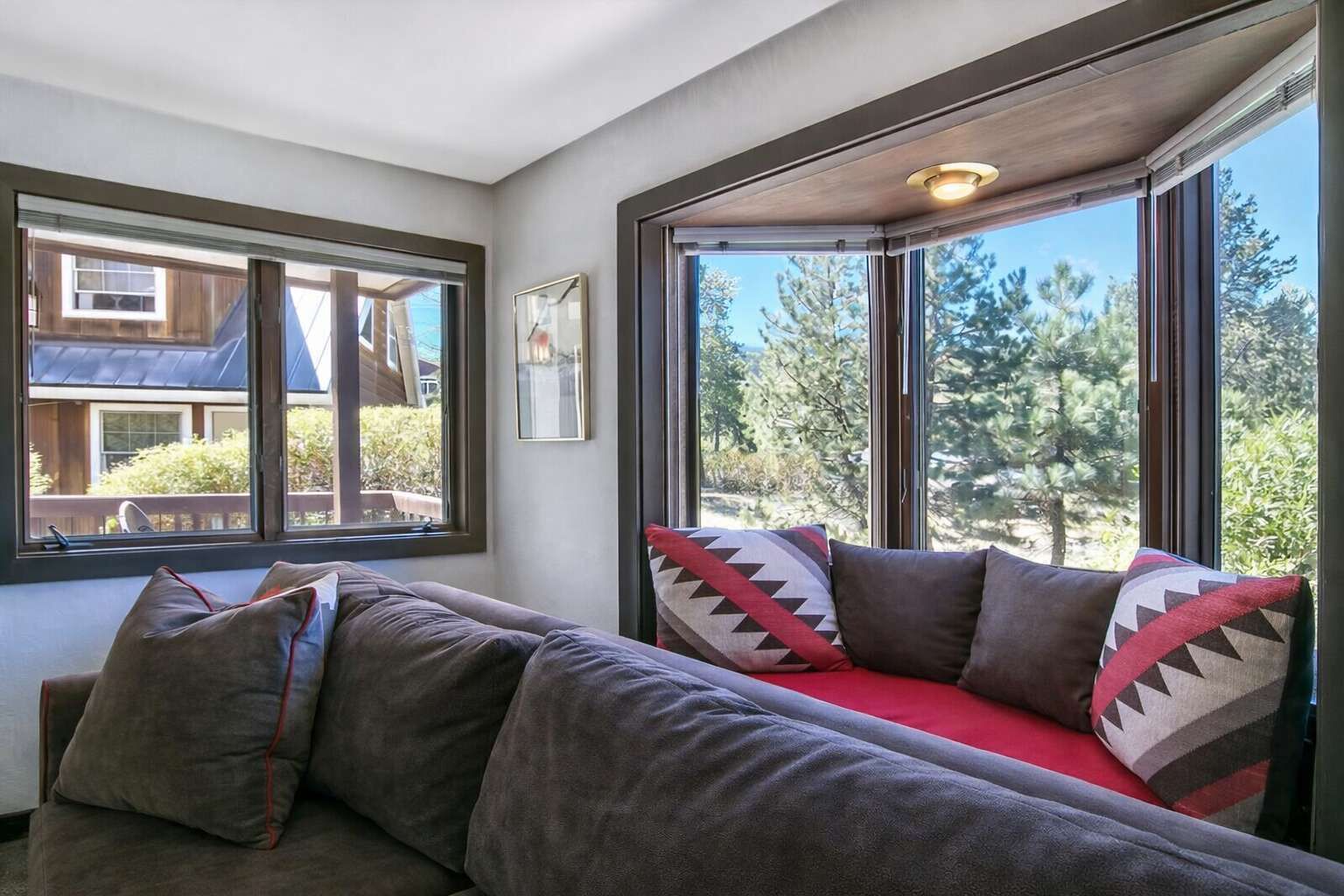 A cozy room with a large window, a cushioned bench, and a framed picture on the wall.