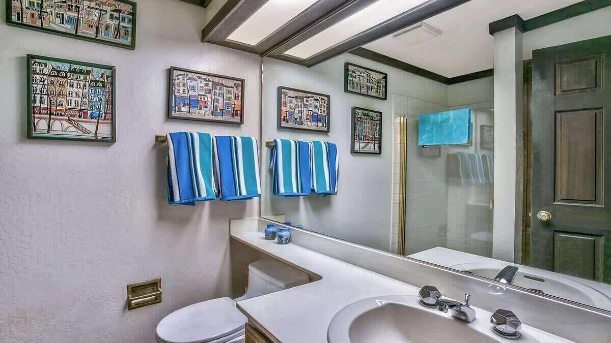 Un baño con un lavabo blanco, un espejo y toallas azules colgadas en la pared.