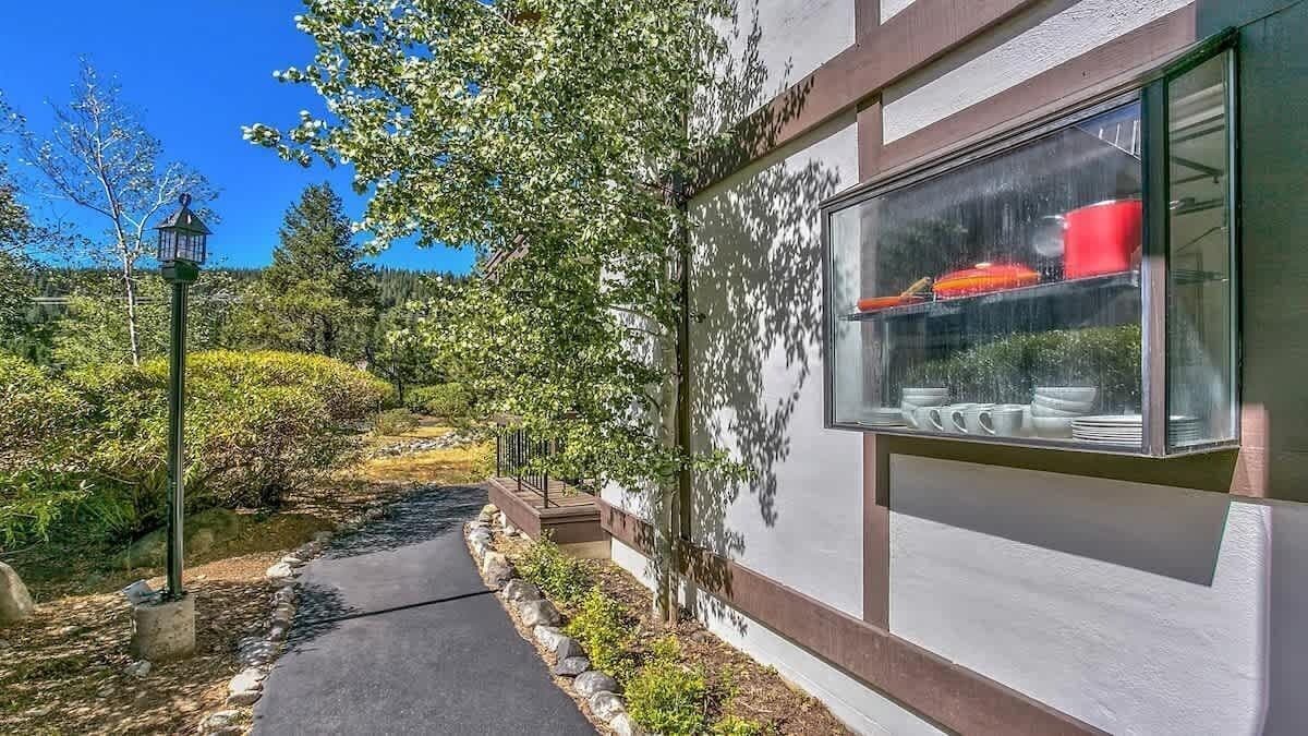 Un chemin menant à un bâtiment dont la fenêtre, en verre, expose des ustensiles de cuisine.