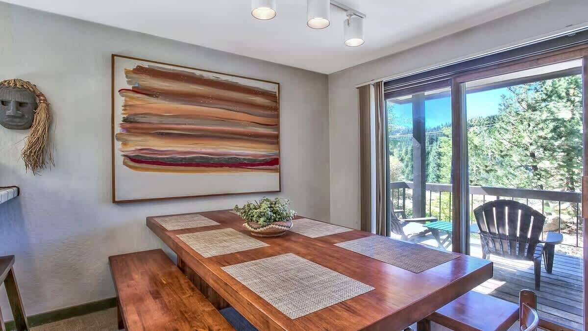 A wooden dining table with placemats, a large abstract painting, and a view of the outdoors through a glass door.
