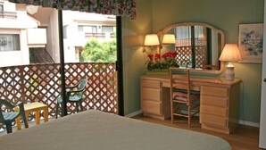 A bedroom with a bed, a wooden dresser with a mirror, two chairs, and a balcony with a lattice fence. - 2 bdr, 2.5 bath, Townhouse Style Condo, Pool (Avalon)