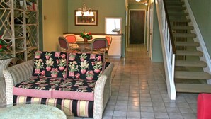 A dining area with a table and chairs, a staircase, and a wicker sofa with a floral cushion. - 2 bdr, 2.5 bath, Townhouse Style Condo, Pool (Avalon)