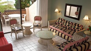 A cozy living area with wicker furniture, a glass coffee table, and a sofa with floral cushions. There are two wall-mounted lamps and a mirror above the sofa. - 2 bdr, 2.5 bath, Townhouse Style Condo, Pool (Avalon)