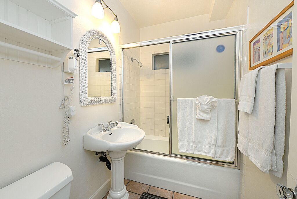 A bathroom with a pedestal sink, a large mirror, a shower enclosure, and a toilet.