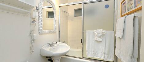A bathroom with a pedestal sink, a large mirror, a shower enclosure, and a toilet.