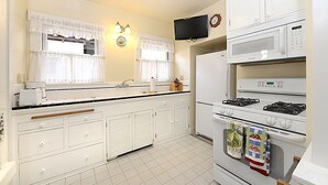 Une cuisine avec des meubles blancs, un four à micro-ondes, une cuisinière et un téléviseur fixé au mur.