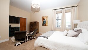 A bedroom with a large bed, a chair, a wooden cabinet, a painting, and a chandelier.
