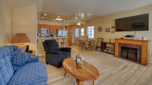 A spacious living room with a sofa, armchair, and coffee table. A fireplace and TV are mounted on the wall.