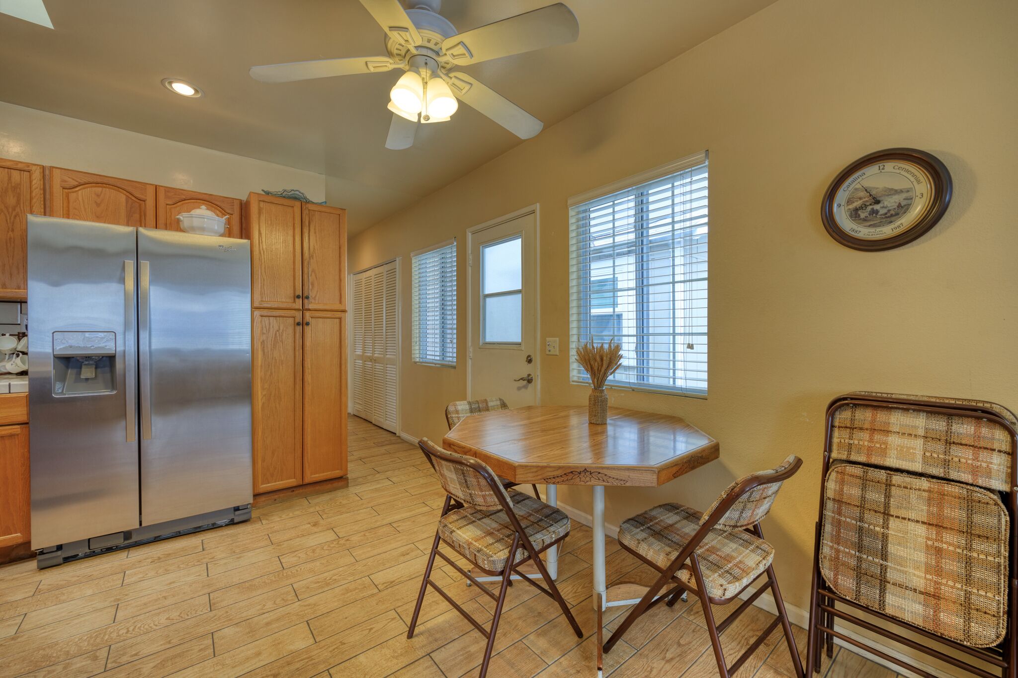 A kitchen with wooden cabinets, a stainless steel refrigerator, a dining table with chairs, and a ceiling fan.