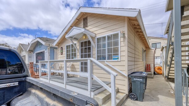 A two-story house with a porch, a covered entryway, and a visible trash bin.