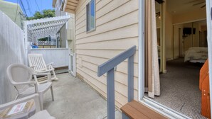 A small, single-story building with a covered porch, a wooden bench, and a pair of white plastic chairs.