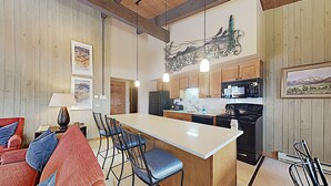 Una cocina moderna con armarios de madera, una isla central, taburetes de bar y un comedor con sillas rojas y azules.