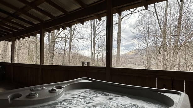Ein Whirlpool mit Blick auf eine bewaldete Landschaft durch große Fenster.